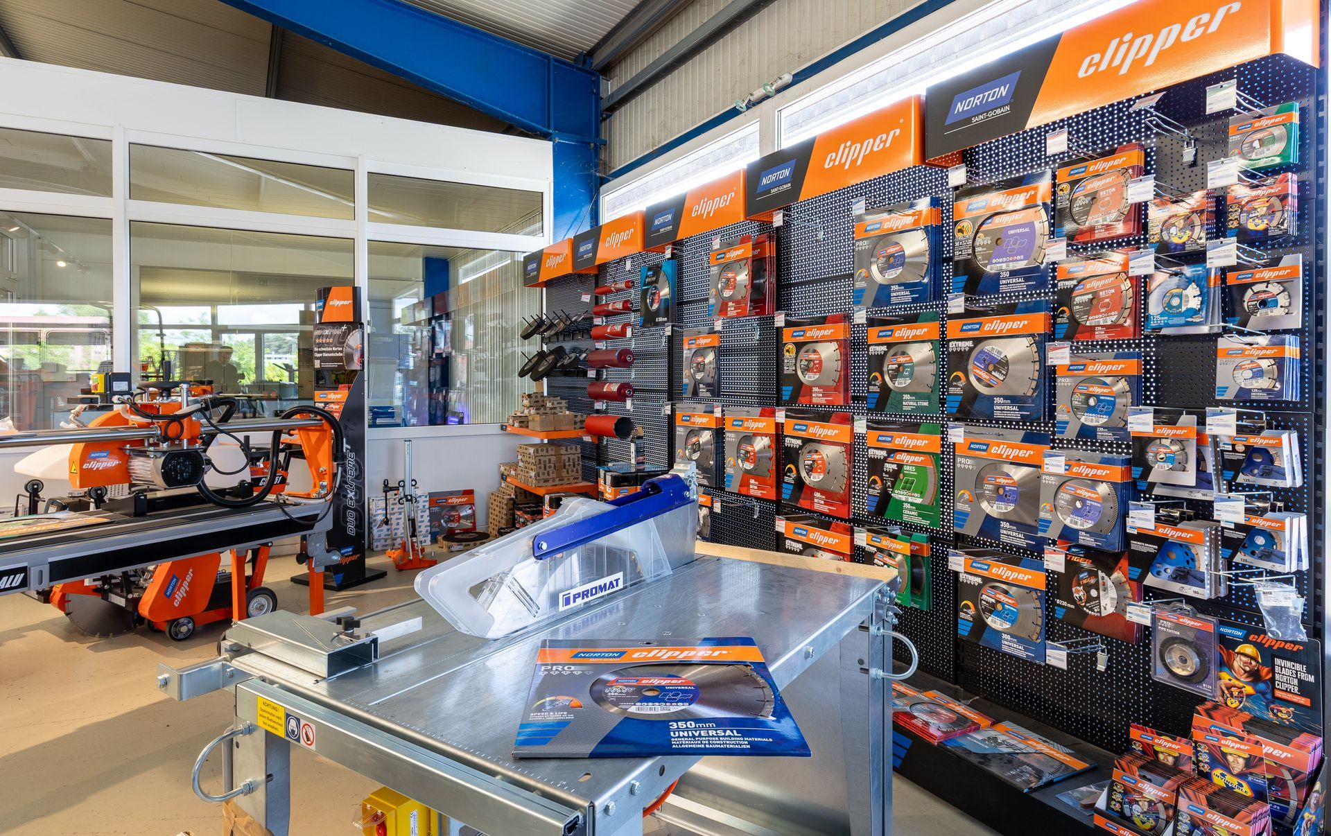 Gang im Baumarkt mit orange-schwarzen Werkzeugauslagen und einer zentralen Werkbank aus Metall.