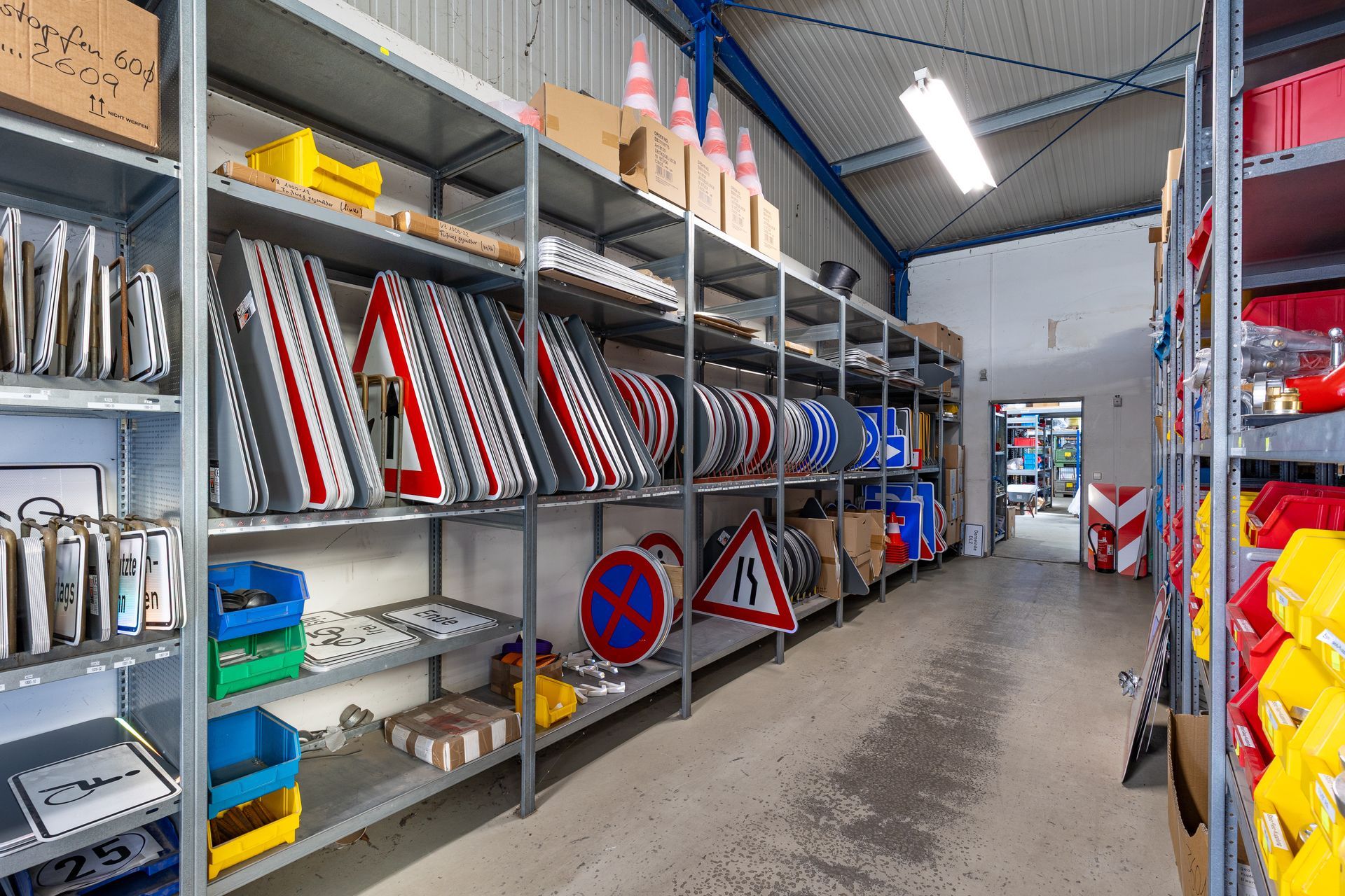 Industrielagergang mit Metallregalen, die mit Verkehrsschildern, Kegeln und verschiedenen Zubehörteilen bestückt sind