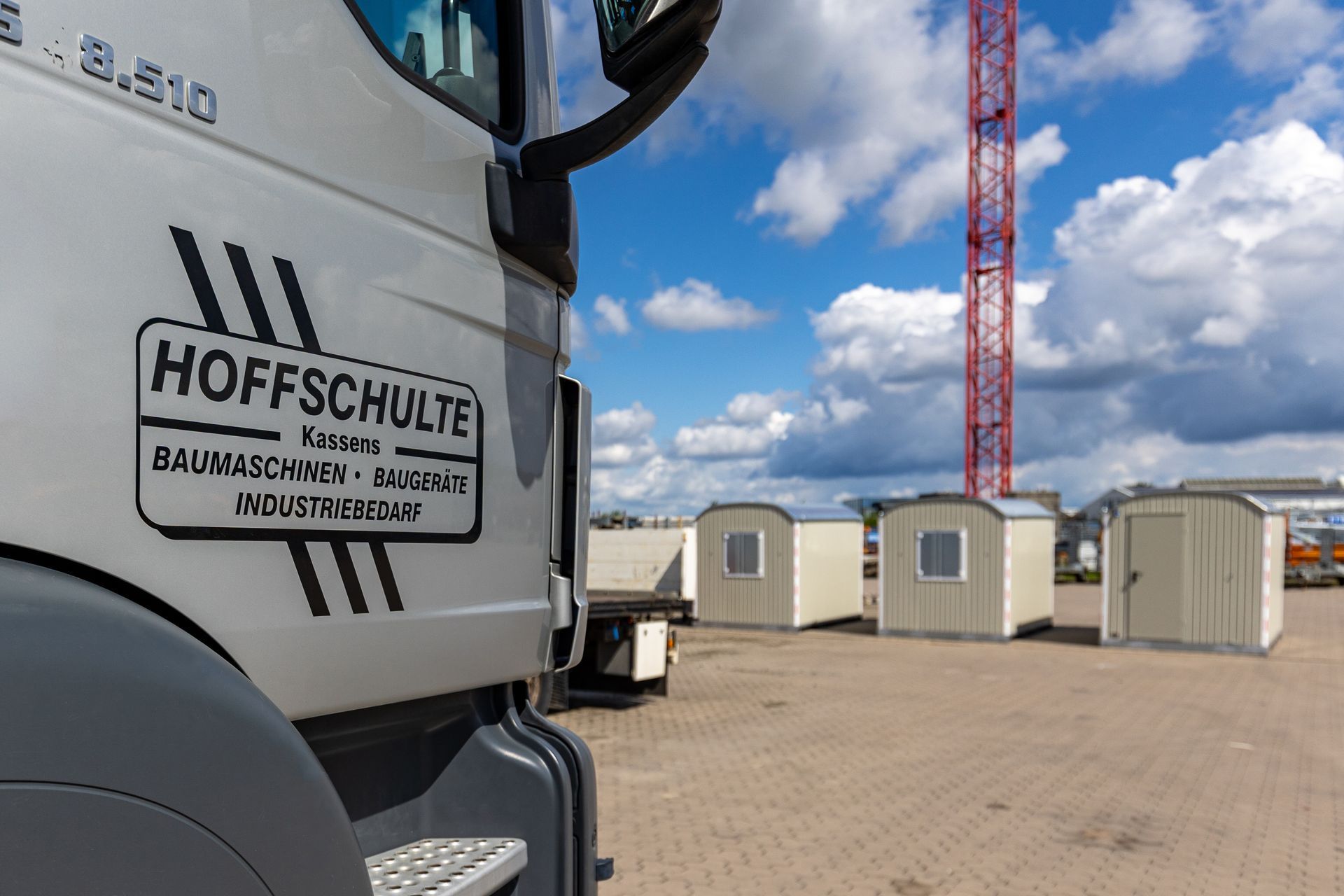 Ein Hoffschulte-Lkw neben modularen Baustellenbüros unter blauem Himmel mit einem roten Kran im Hintergrund