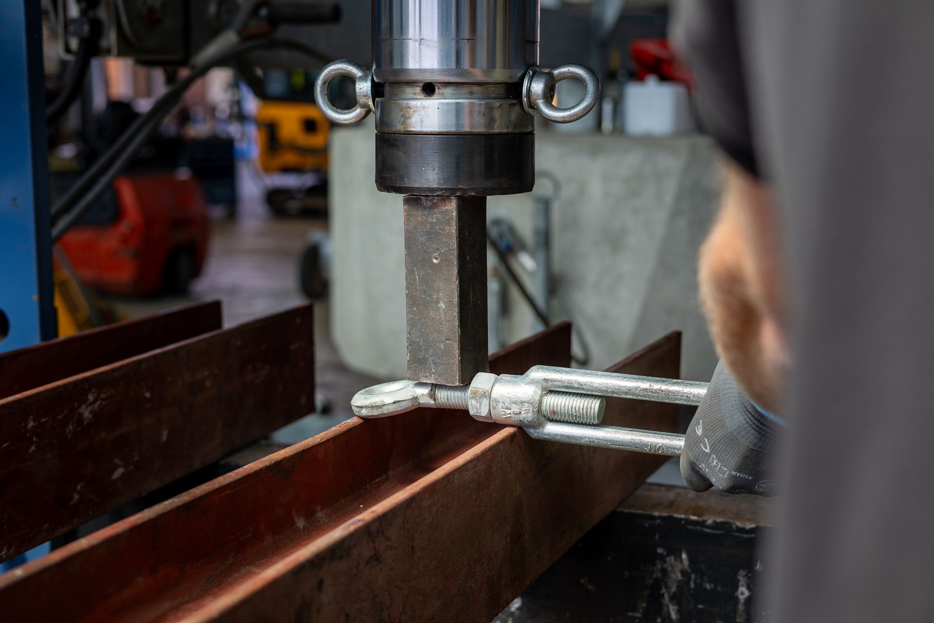 Eine Metallbearbeitungspresse formt ein Stahlstück in einer Werkstatt; im Vordergrund ist ein Handwerkzeug zu sehen.