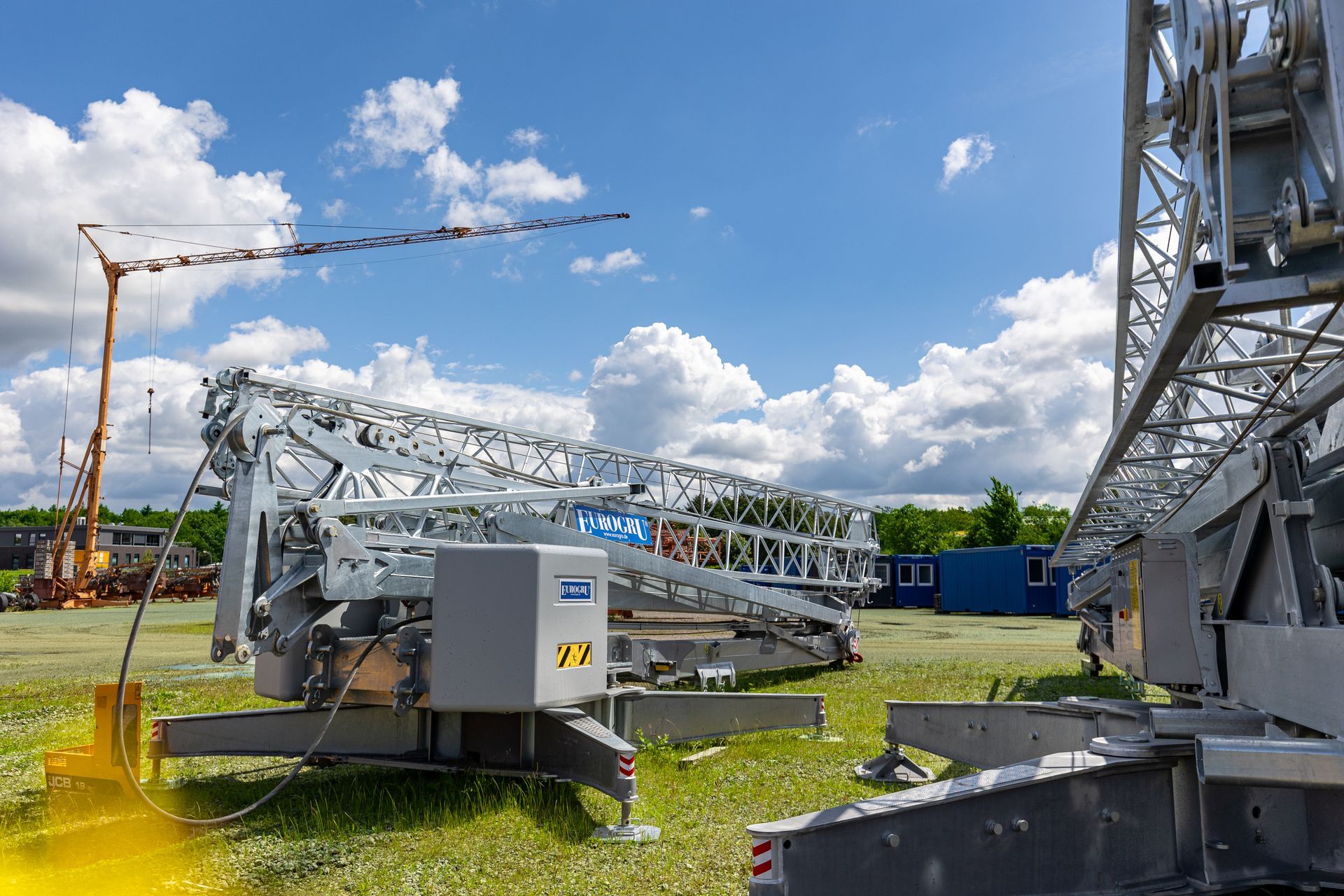 Industriekran auf grasbewachsenem Gelände unter blauem Himmel mit Wolken