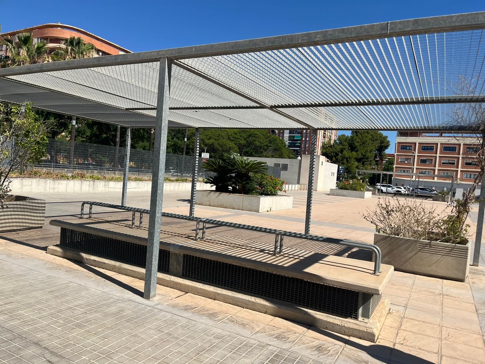 Un banco bajo un dosel en un parque con un edificio al fondo.