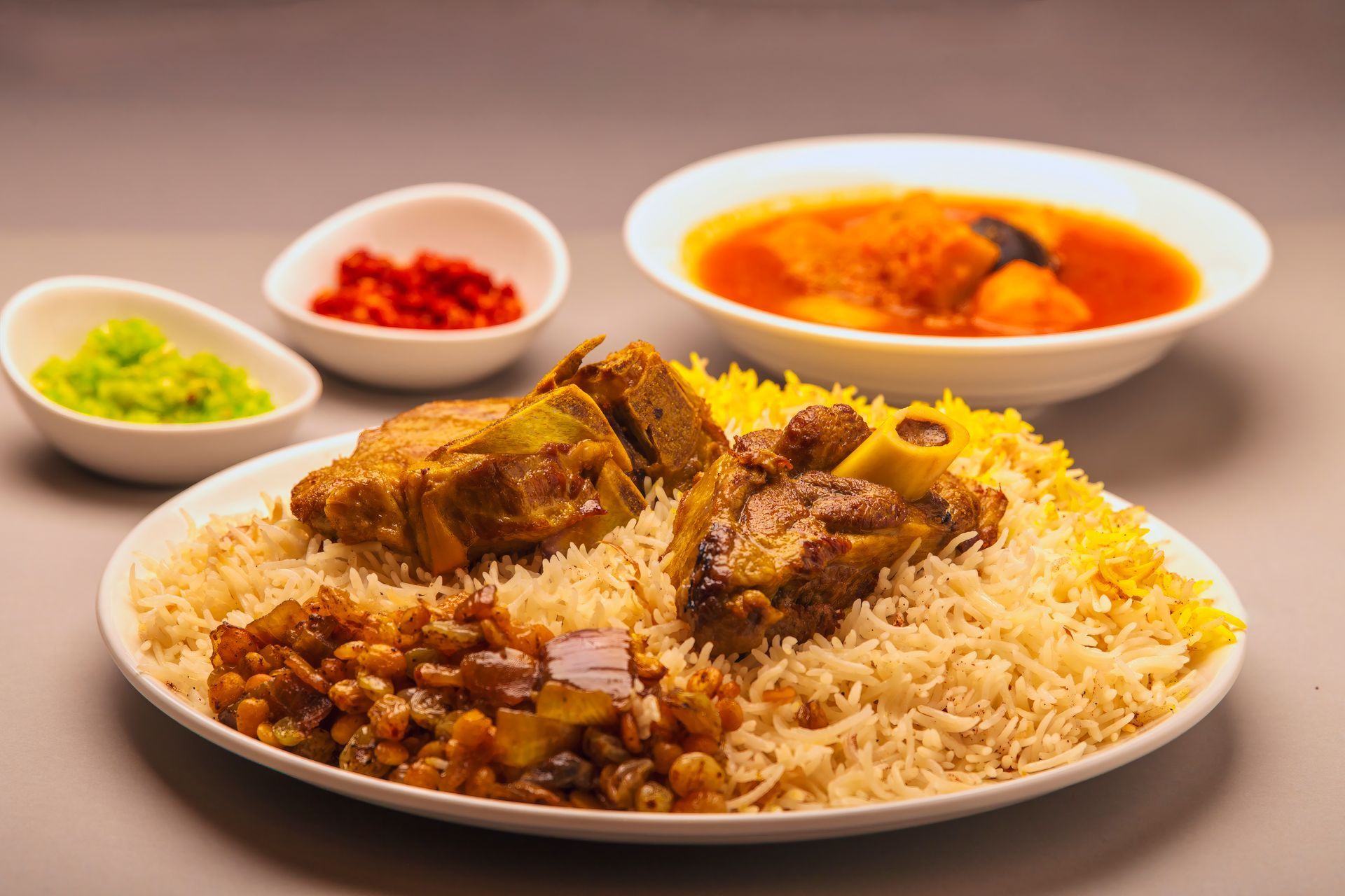 Assiette de biryani avec des morceaux de viande, servie avec trois sauces d'accompagnement colorées sur une table