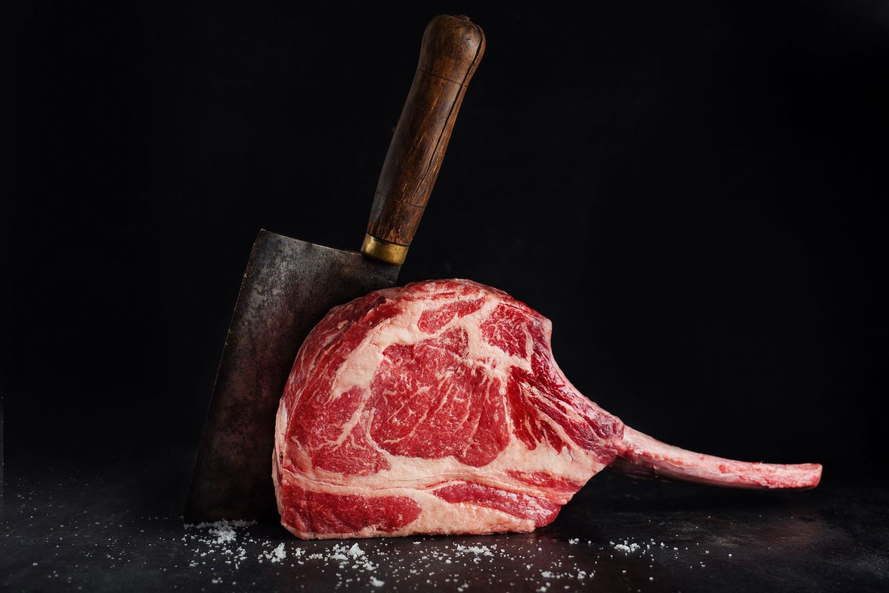 Un steak persillé cru à côté d'un couperet à viande sur fond sombre