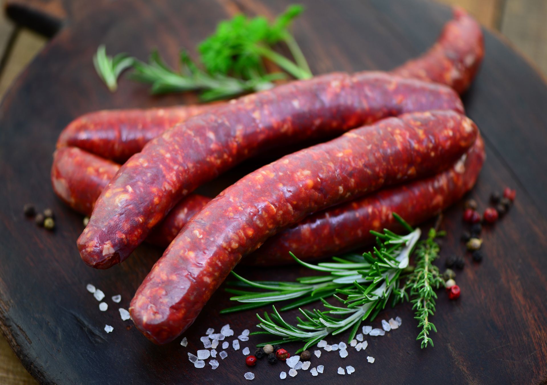 Merguez sur une planche à découper foncée avec du romarin et des grains de poivre.