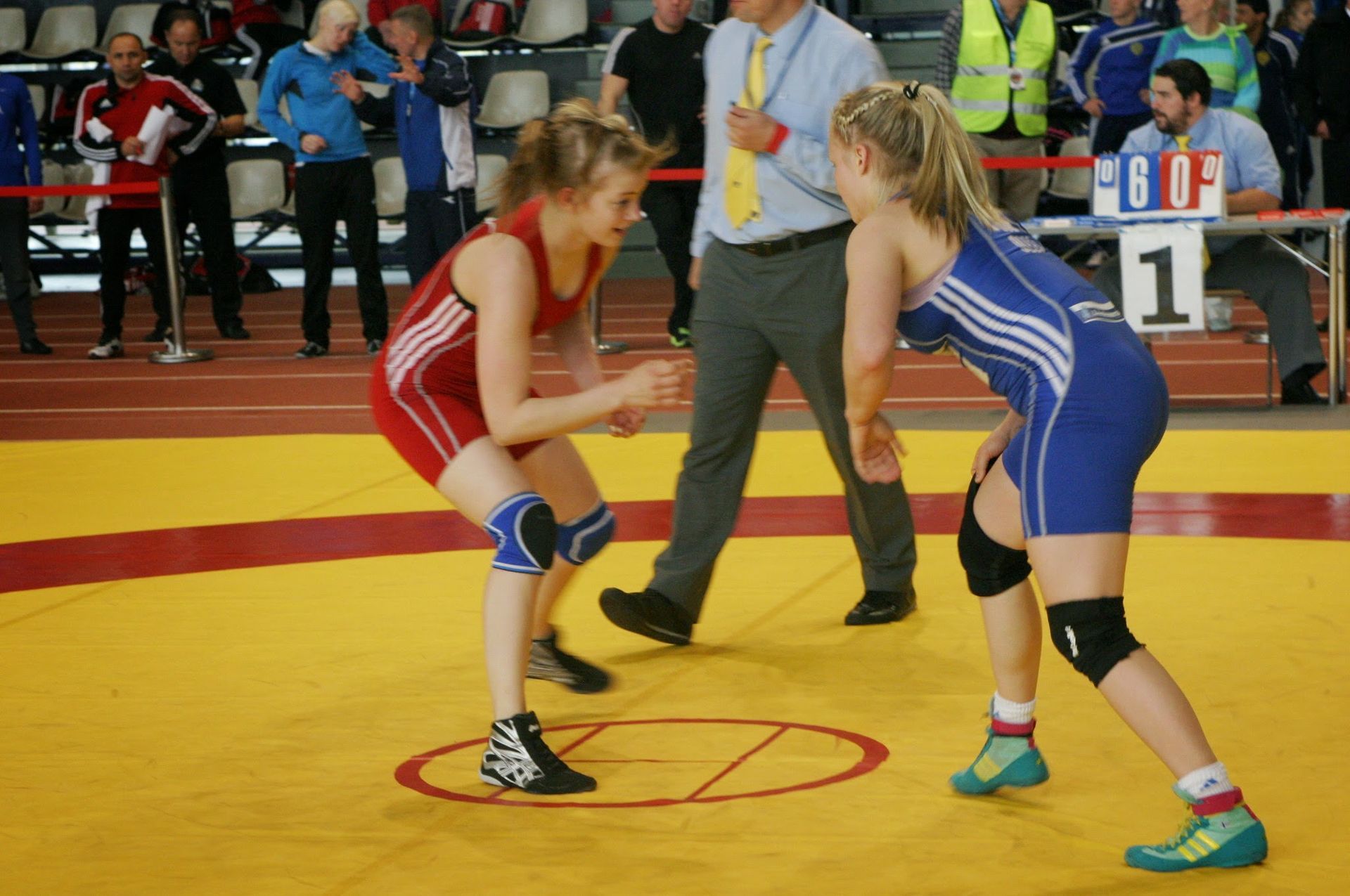 Kaksi puna-sinipaidassa olevaa painijaa seisoo kasvotusten keltaisella matolla ottelun aikana.