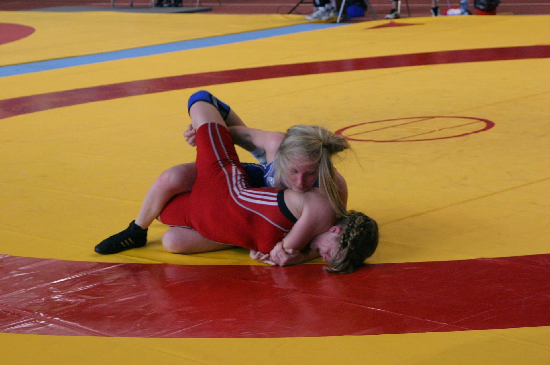 Kaksi painijaa painii keltaisella ja punaisella matolla kilpailullisen ottelun aikana.