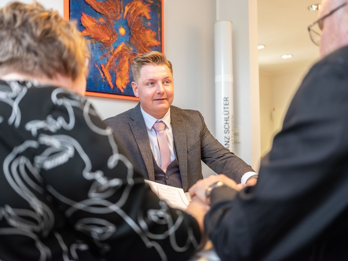 Ein Mann in Anzug und Krawatte sitzt mit zwei Frauen an einem Tisch.