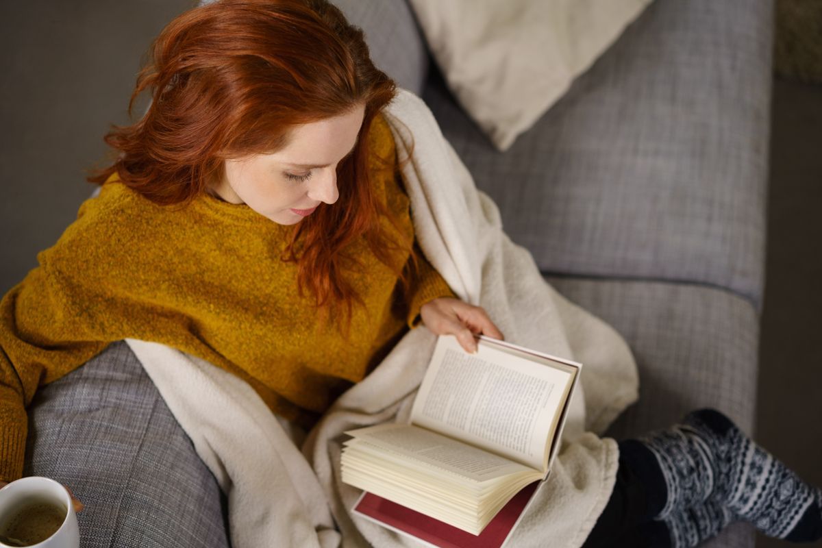 Eine Frau sitzt auf einem Sofa und liest ein Buch.