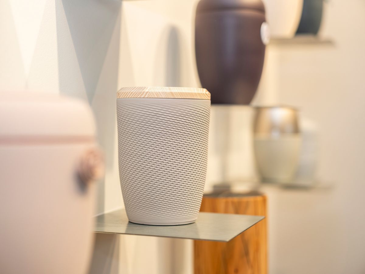 Eine weiße Urne steht auf einem Metallregal in einem Raum.