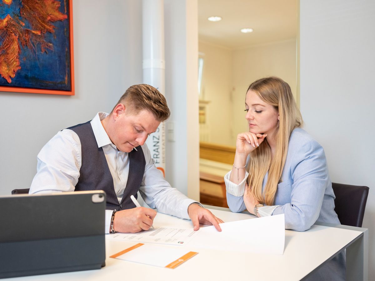 Ein Mann und eine Frau sitzen an einem Tisch und schauen auf ein Tablet.