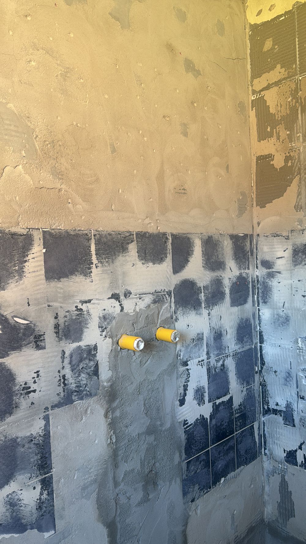 Unfertige Badezimmerwand mit freiliegenden Wasserleitungen und fleckigem Putz.