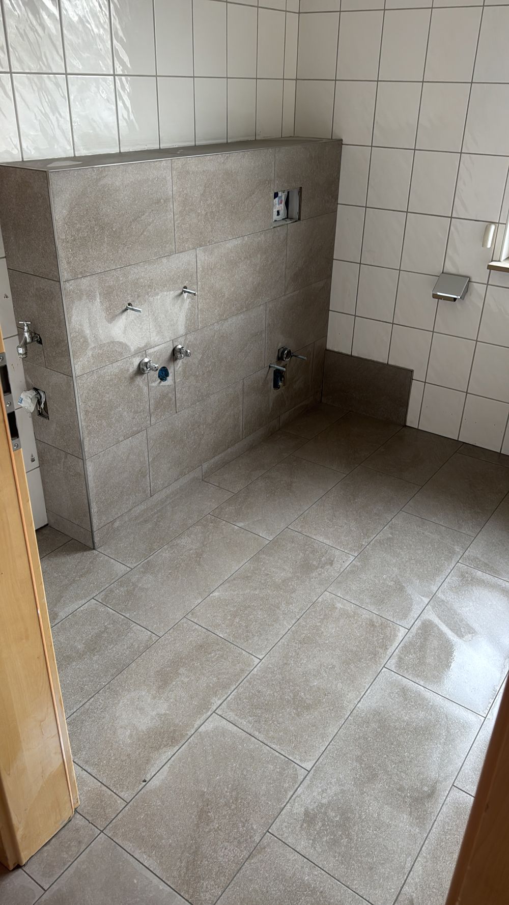 Teilweise gefliestes Badezimmer mit einer großen, an der Wand lehnenden Fliese und unfertigen Sanitärarmaturen.
