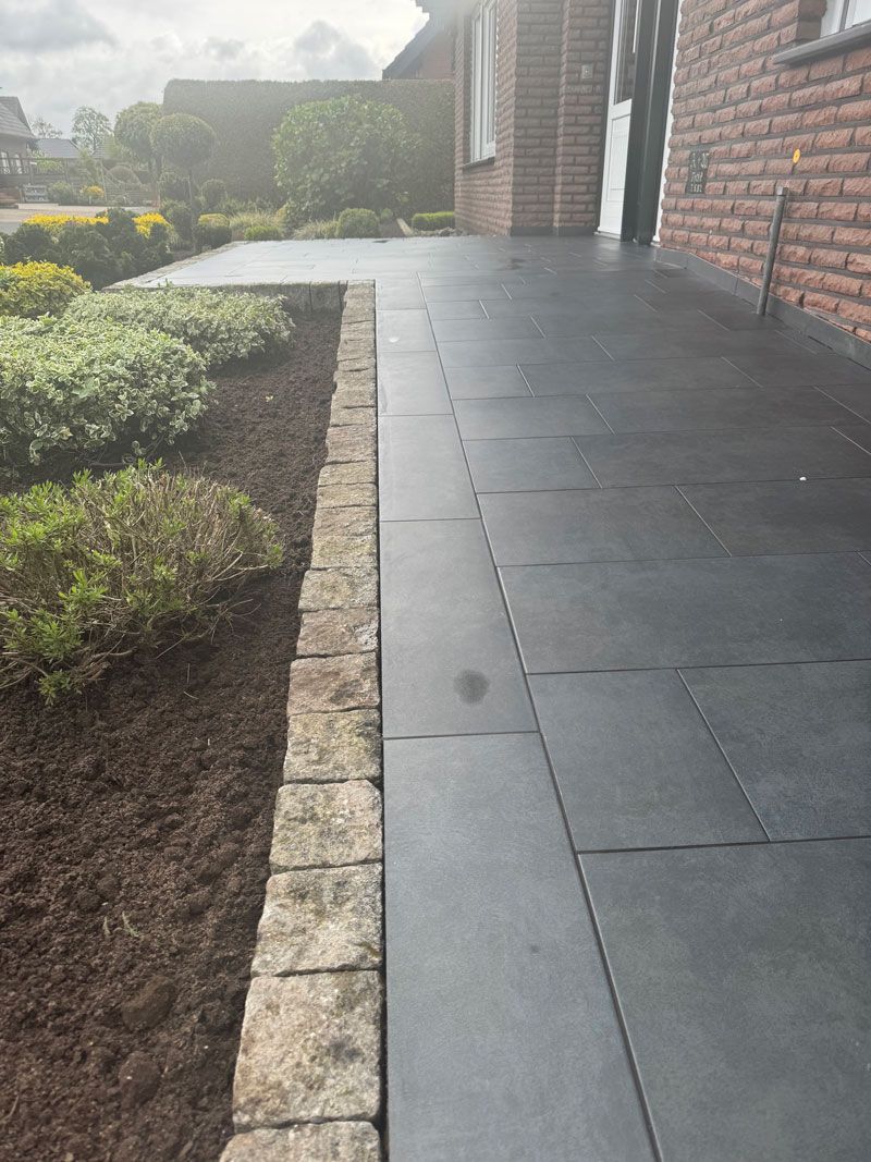 Ein mit schwarzen Fliesen ausgelegter Gehweg führt zu einem Backsteinhaus.