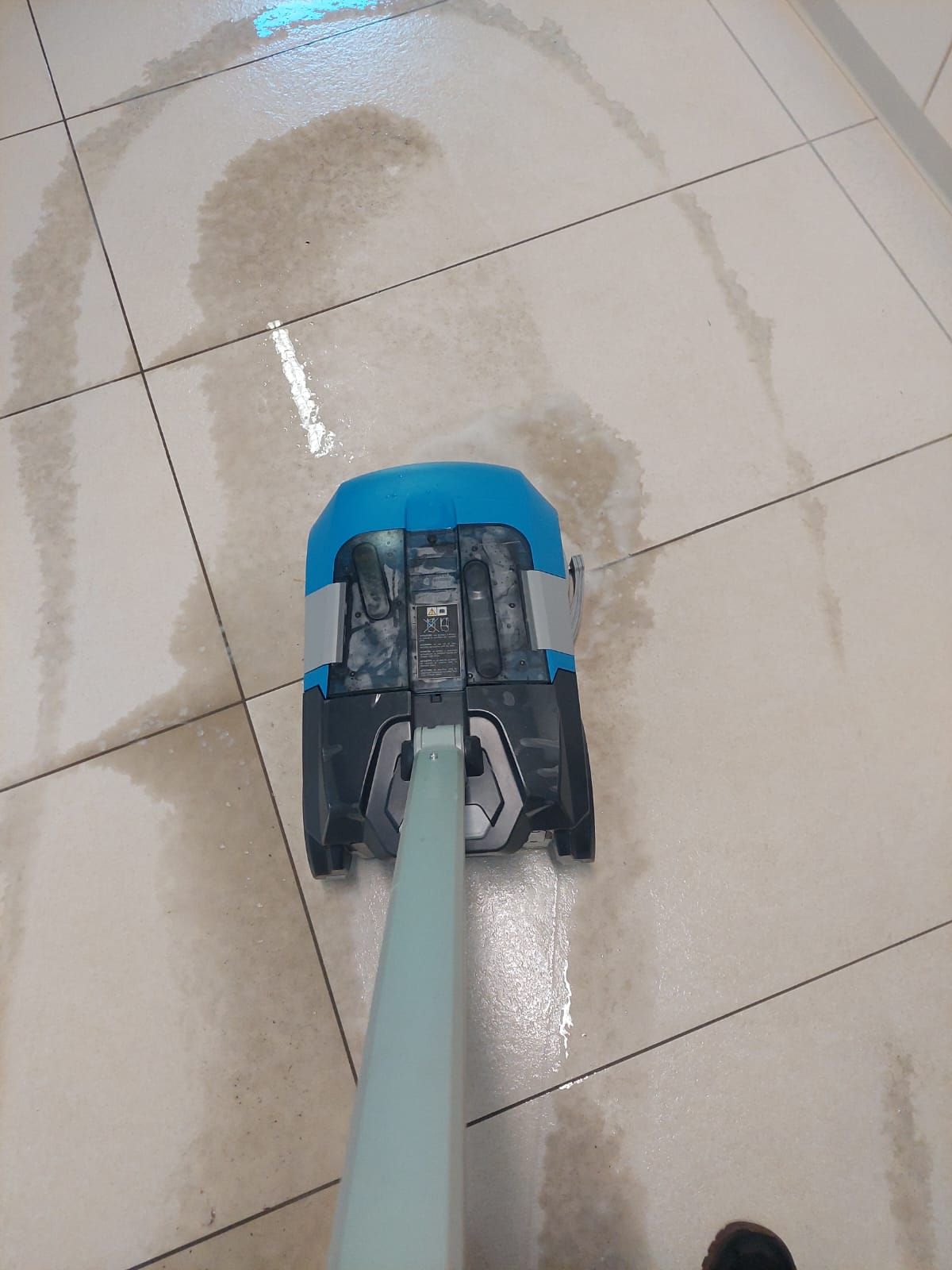 Eine Person reinigt einen gefliesten Boden mit einem Wischmopp.