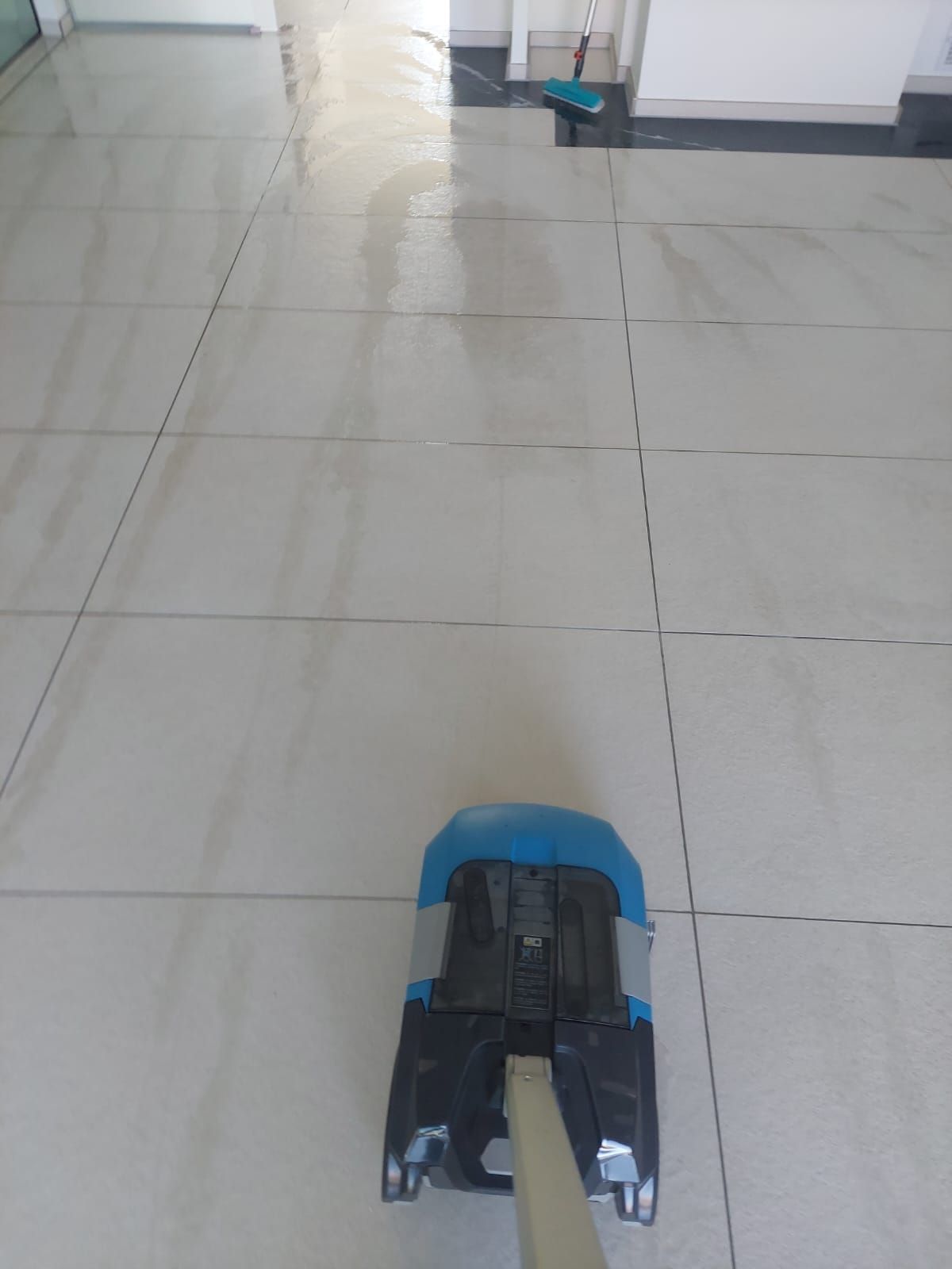 Auf einem gefliesten Boden steht ein Wischmopp neben einem Besen.