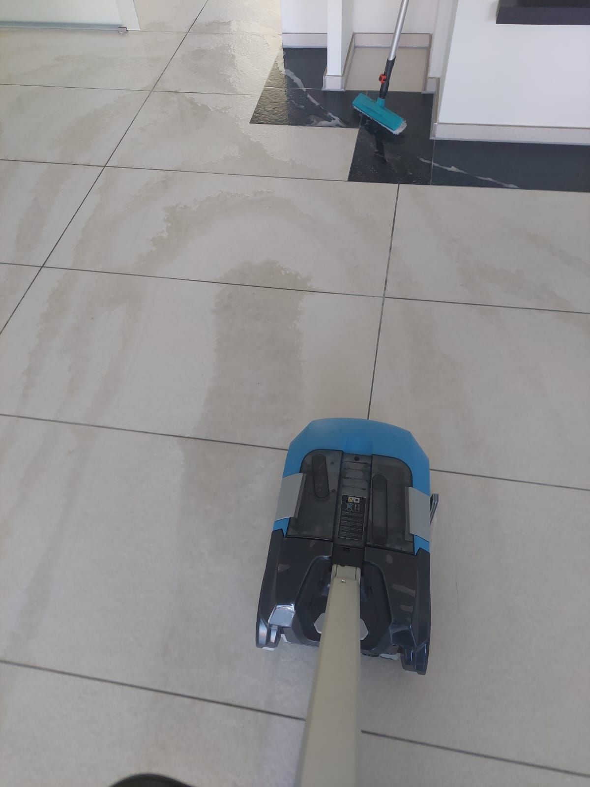 Ein Mopp liegt auf einem gefliesten Boden neben einem Besen