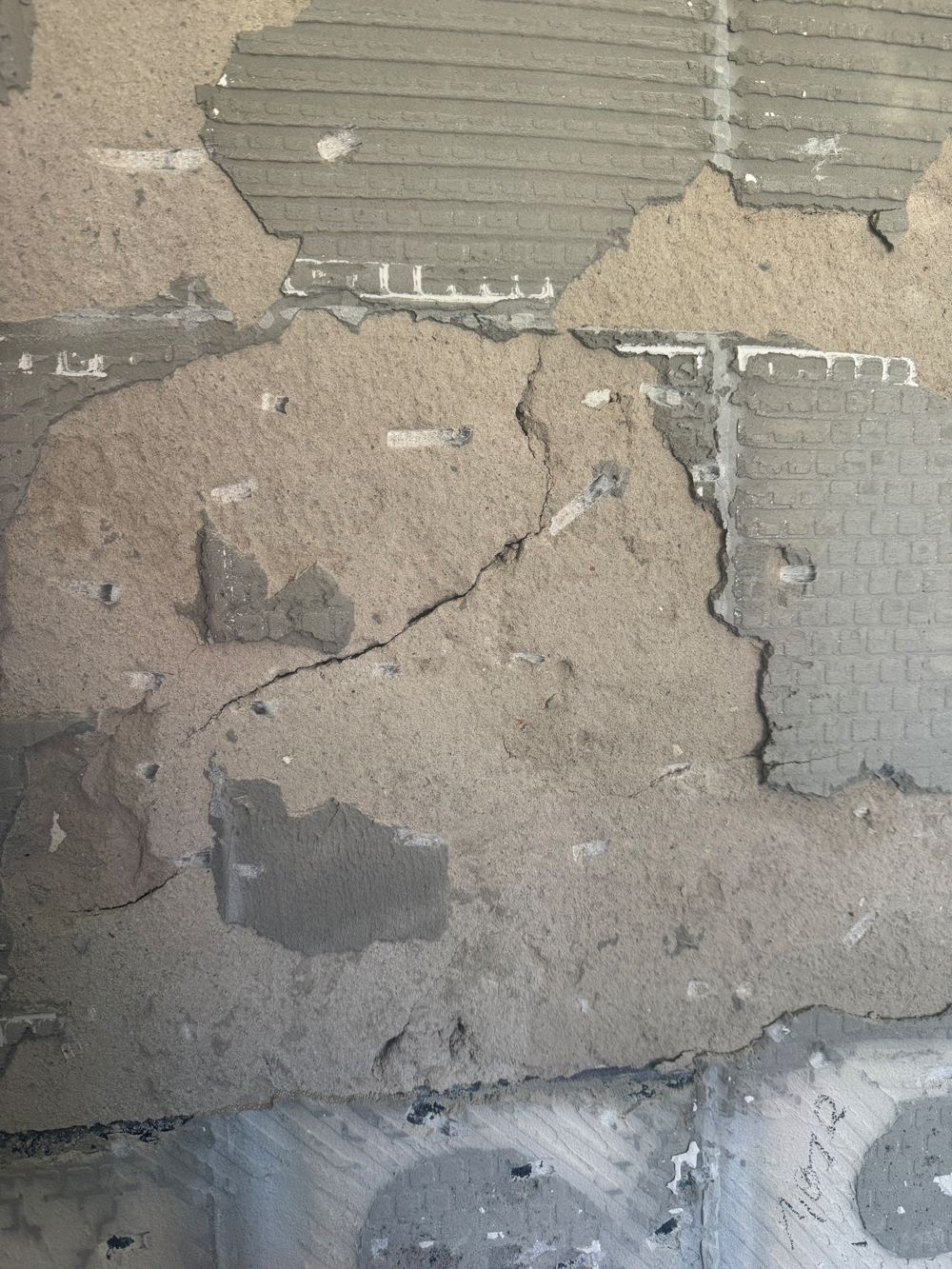 Nahaufnahme von rissigem, abblätterndem Wandputz mit Stellen, an denen graues Material freiliegt.