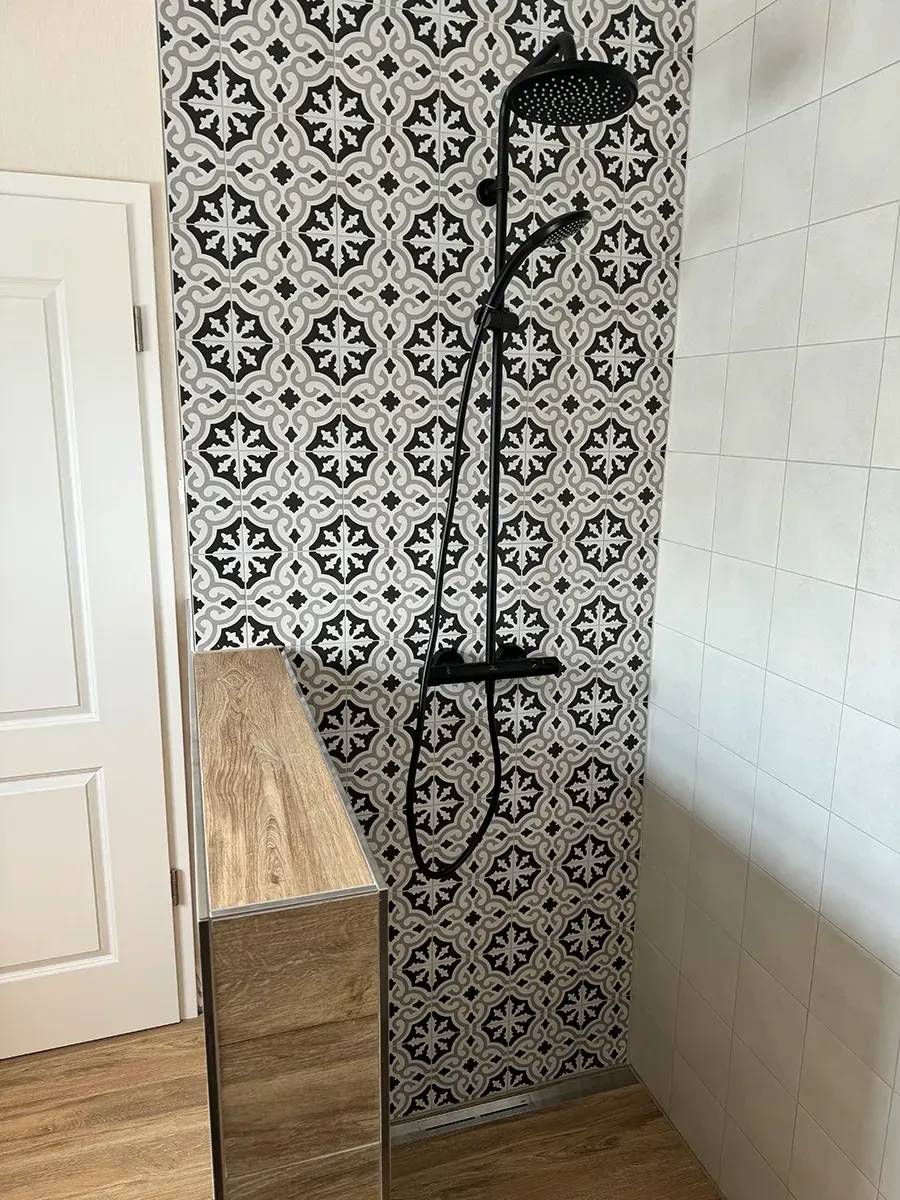 Eine Dusche mit schwarz-weiß gefliester Wand und schwarzem Duschkopf.