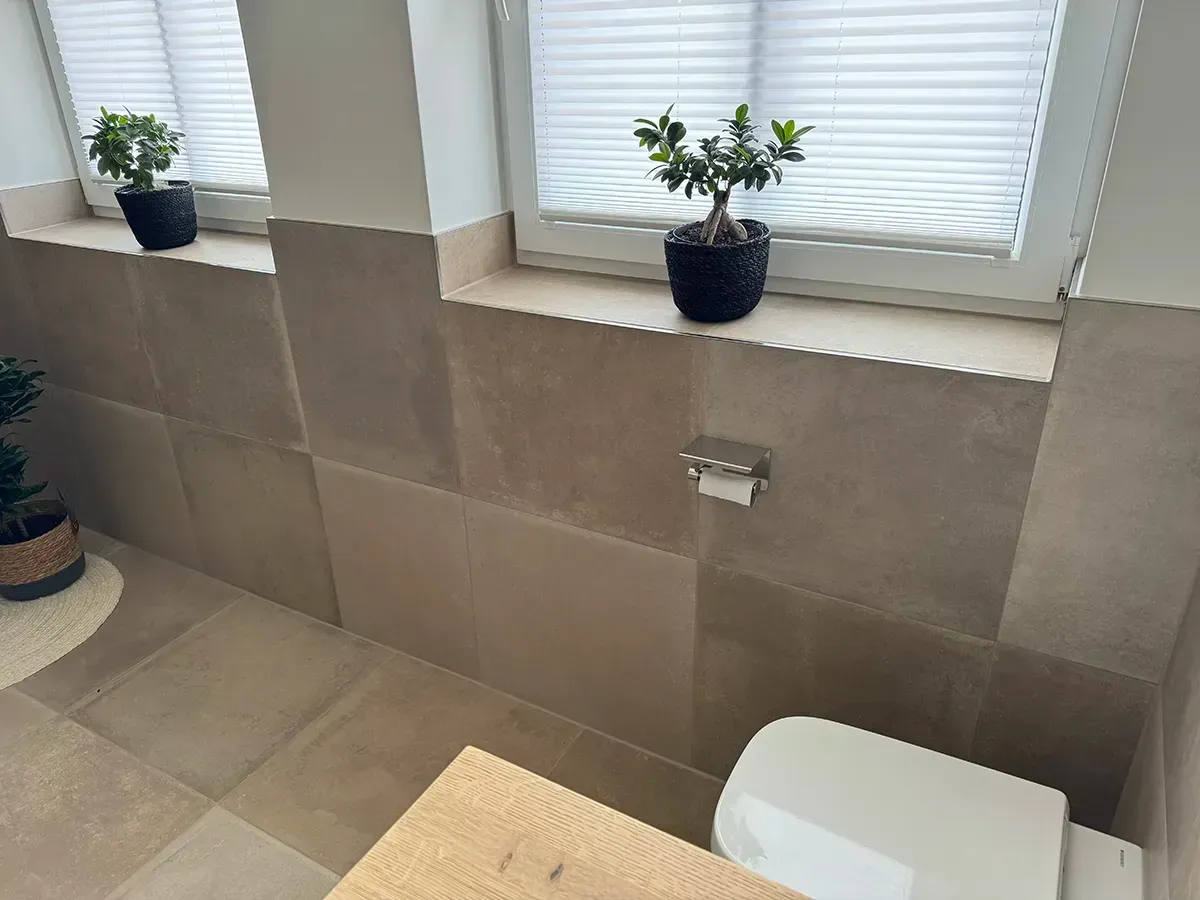 Ein Badezimmer mit Toilette und zwei Topfpflanzen auf der Fensterbank.