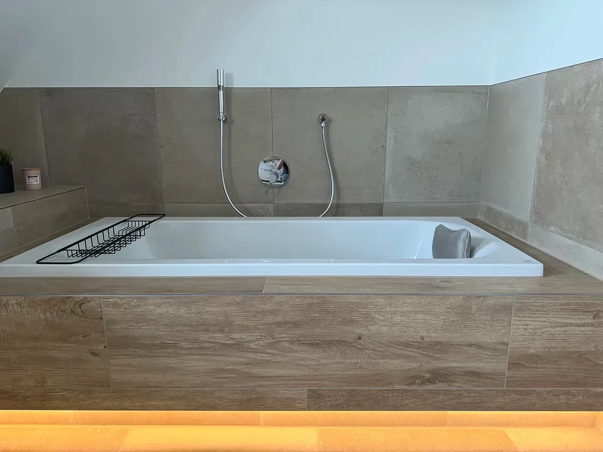 Eine Badewanne in einem Badezimmer mit Holzboden und Duschkopf.