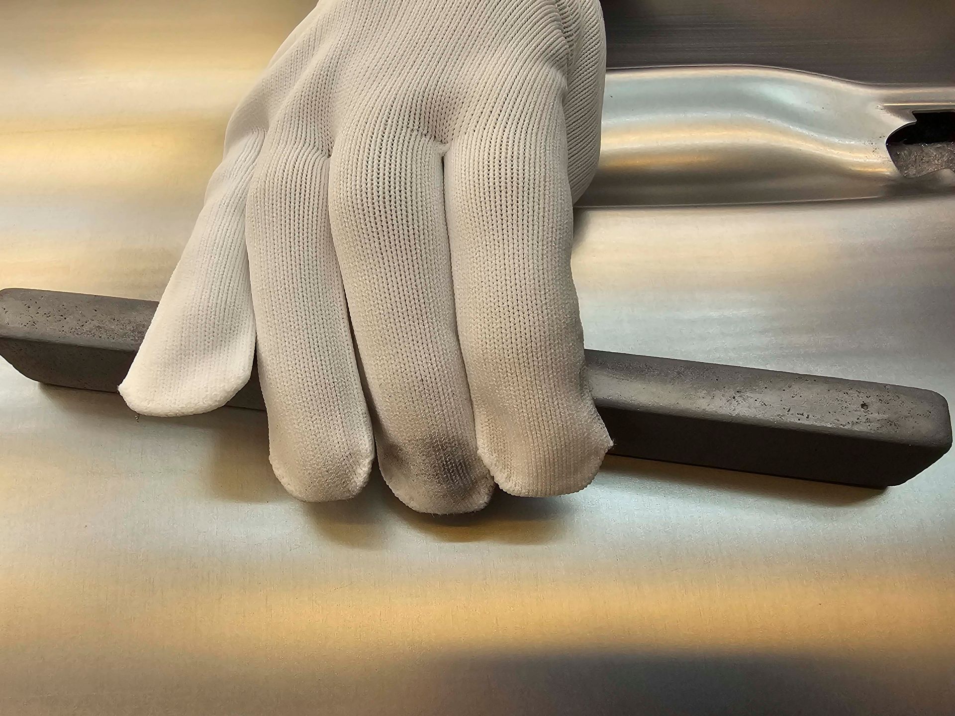 Eine Person mit weißen Handschuhen hält ein Stück Metall in der Hand.
