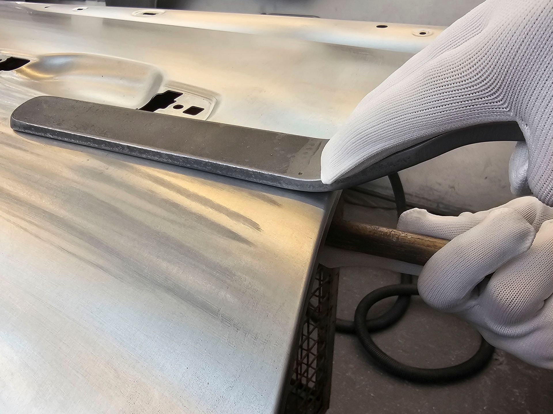 Eine Person mit weißen Handschuhen arbeitet an einem Stück Metall