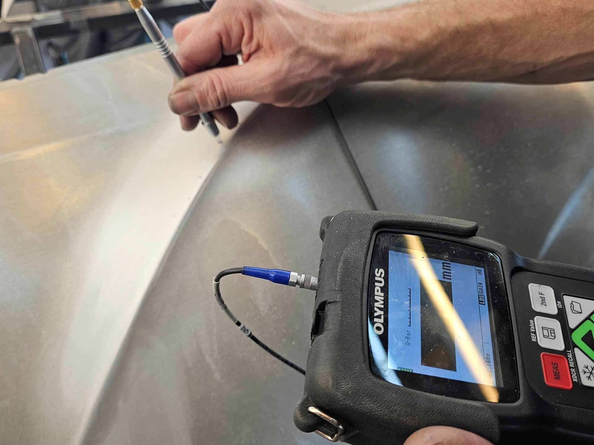 Eine Person misst mit einem Olympus-Gerät eine Metalloberfläche.