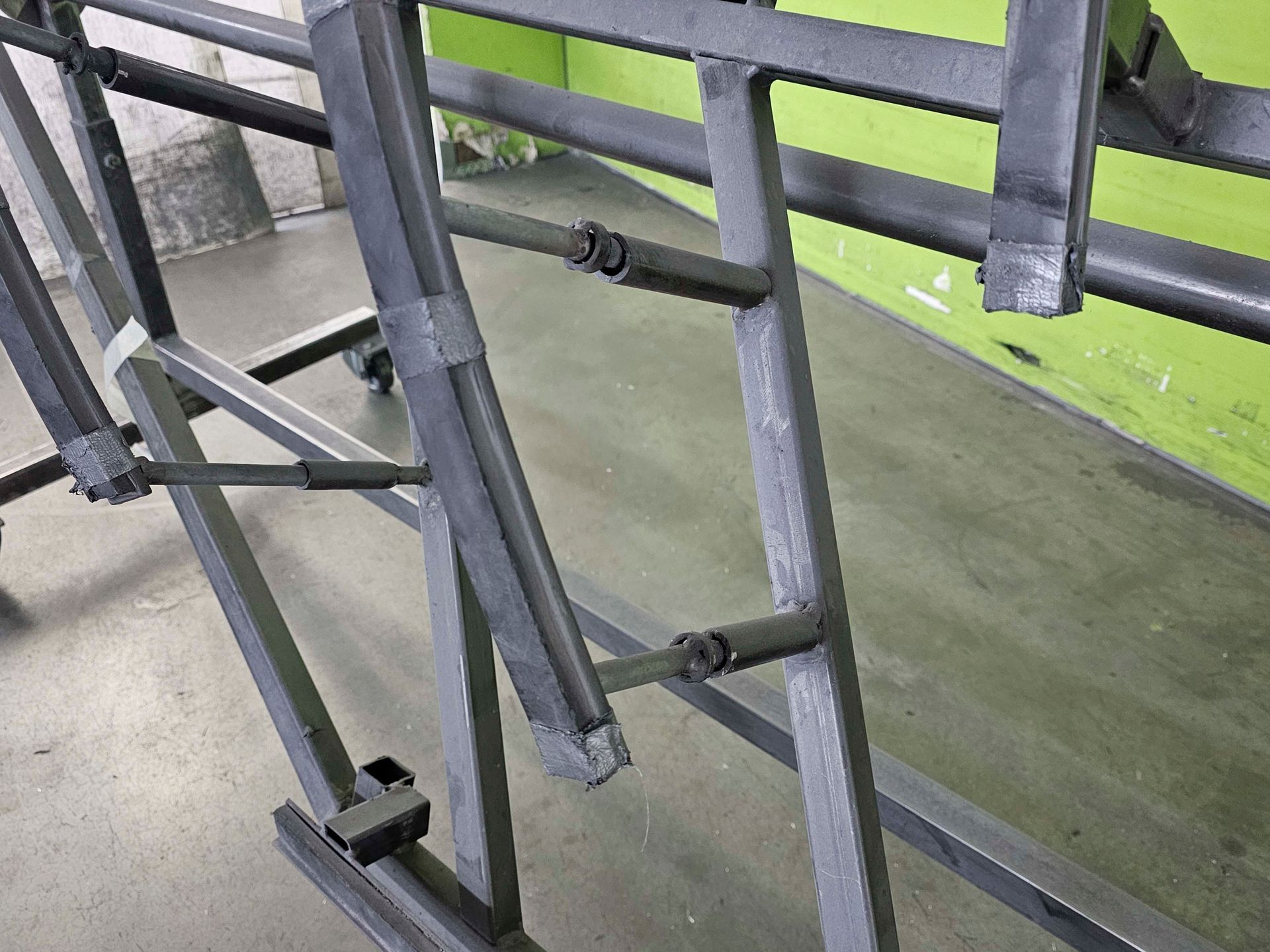 Eine Metallleiter steht auf einem Betonboden vor einer grünen Wand.