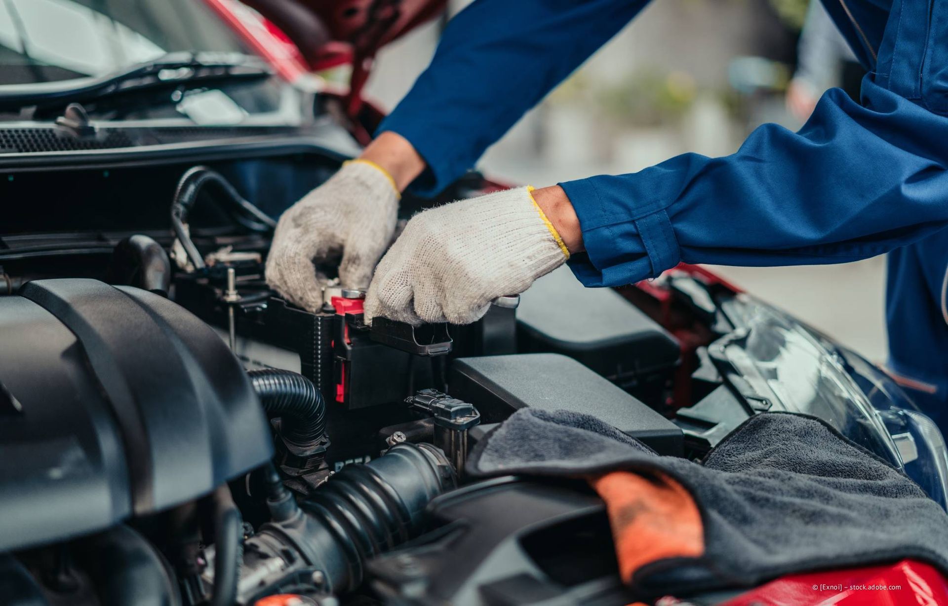Ein Mechaniker im blauen Overall und mit Handschuhen arbeitet an einem Automotor.