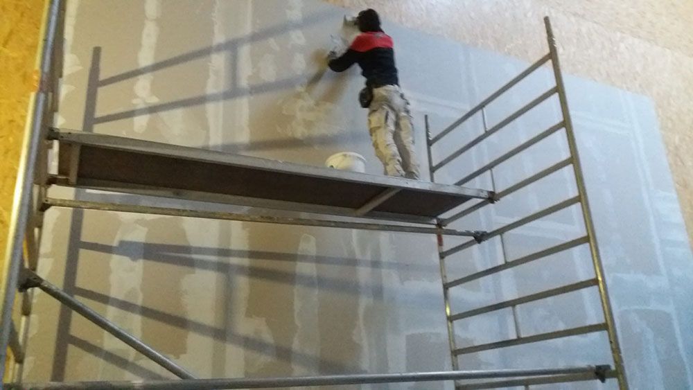 Ein Mann steht auf einem Gerüst und streicht eine Wand.