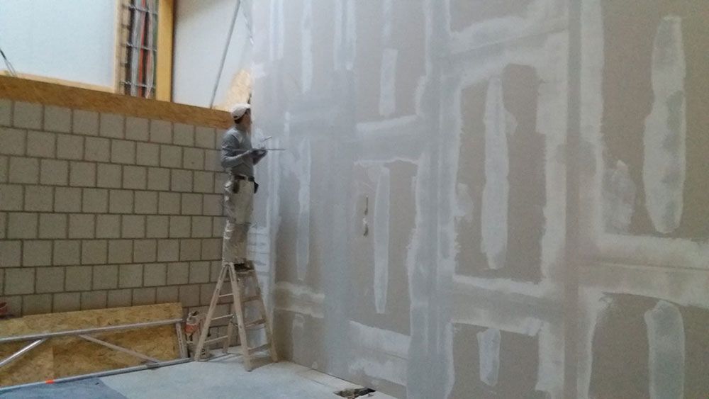 Ein Mann steht auf einer Leiter und streicht eine Wand.