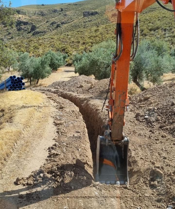 Una excavadora naranja está cavando una zanja en la tierra.