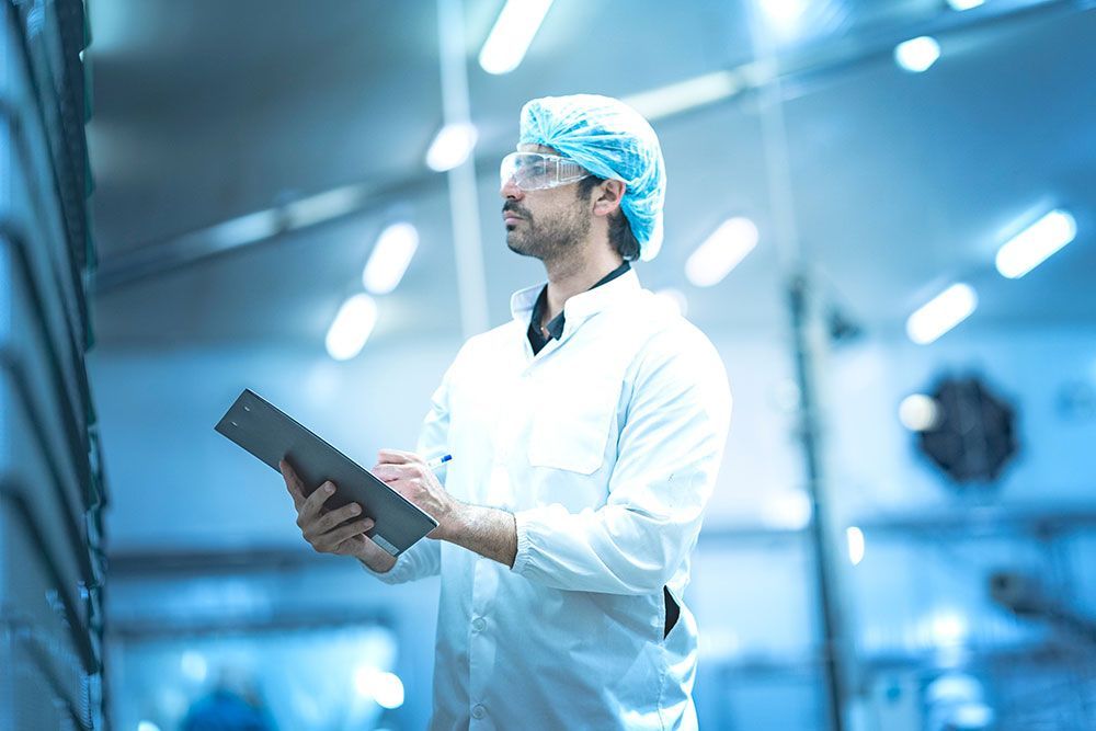 Wissenschaftler im Laborkittel und Haarnetz hält ein Tablet in einem hellen, modernen Labor