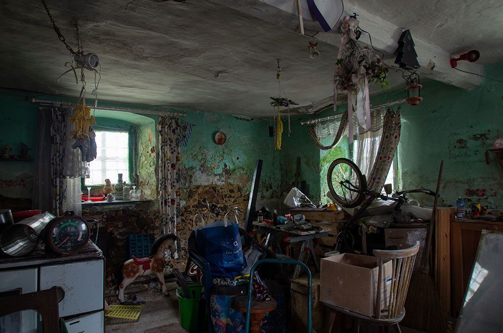 Unordentliche, heruntergekommene Wohnung mit kaputter Decke, verstreuten Möbeln und einem Fahrrad inmitten von Trümmern.