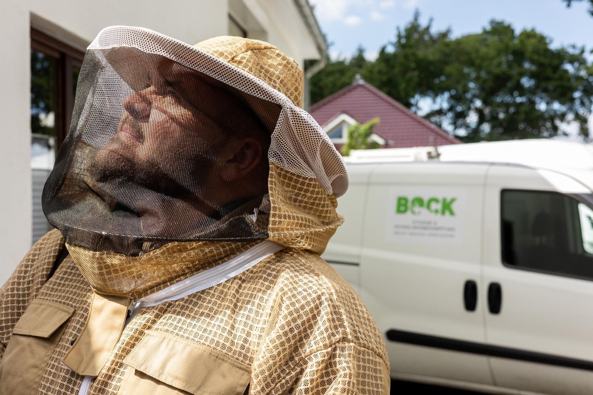 Eine Person in Imkerschutzkleidung steht im Freien neben einem weißen Beck-Lieferwagen.