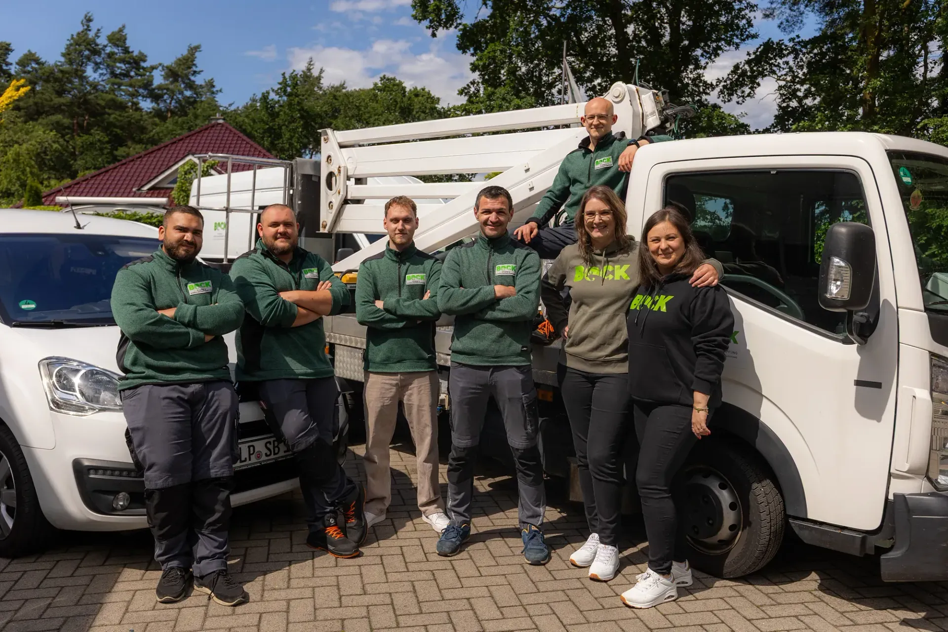 Sechs Personen posieren an einem sonnigen Tag im Freien neben weißen Lieferwagen.
