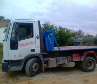 Un camión blanco con plataforma azul está estacionado en un camino de tierra.