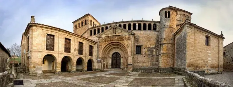 Fachada de piedra de una iglesia con entradas en arco y un campanario en un patio histórico