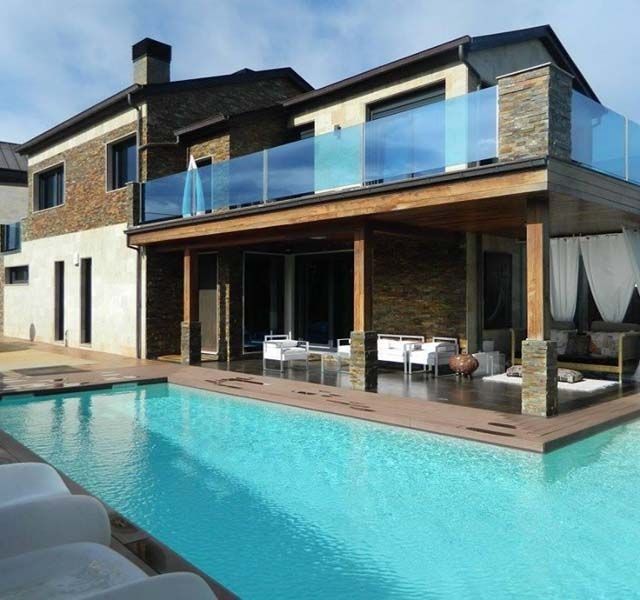 Villa moderna de dos plantas con piscina turquesa, balcón de cristal y patio cubierto junto al agua