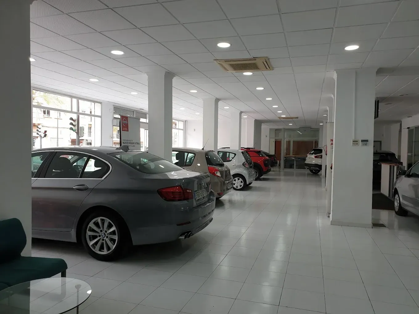 Autos estacionados en una sala de exposición de un concesionario de automóviles bien iluminada, con pisos, paredes y techo blancos.