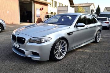 Eine silberne BMW M5 Limousine parkte auf einem Parkplatz vor einem Gebäude.