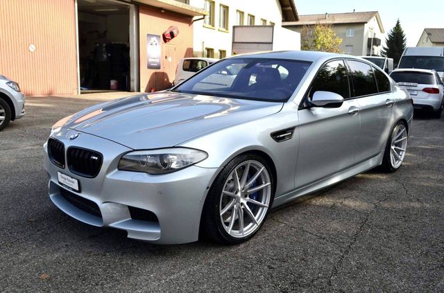 Eine silberne BMW M5 Limousine parkte auf einem Parkplatz vor einem Gebäude.