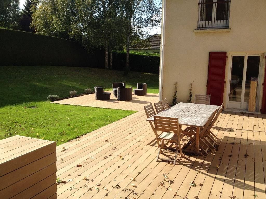 Terrasse en bois avec table à manger et coin salon donnant sur une pelouse verdoyante et des arbres.