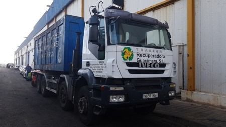 Un camión blanco con un contenedor de basura azul está estacionado frente a un edificio.