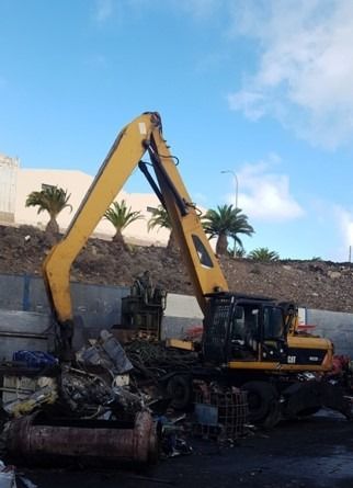 Una gran excavadora amarilla está encima de una pila de chatarra.