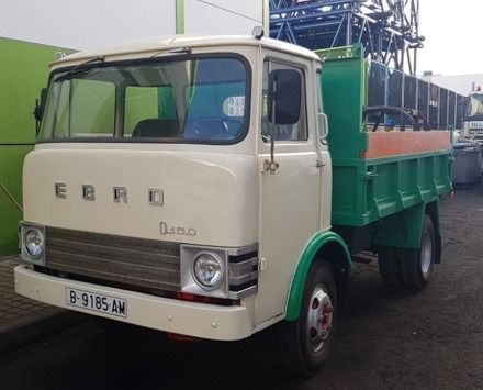 Un camión blanco con una caja verde está estacionado frente a un edificio.