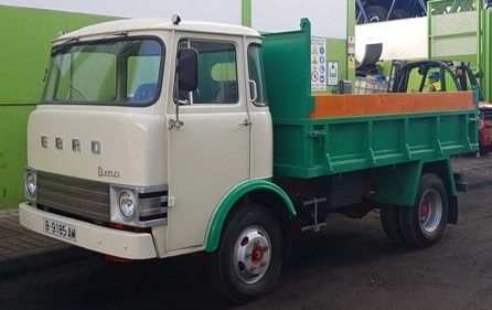 Un camión volquete blanco y verde está estacionado frente a un edificio verde.