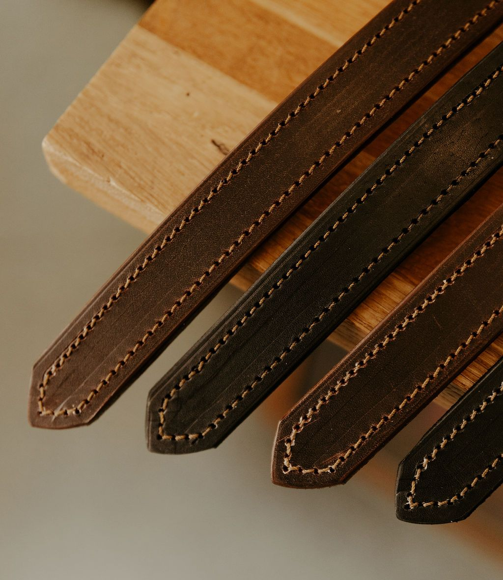 Quatre lanières de cuir aux bords cousus, de nuances de brun variées, sur une surface en bois.