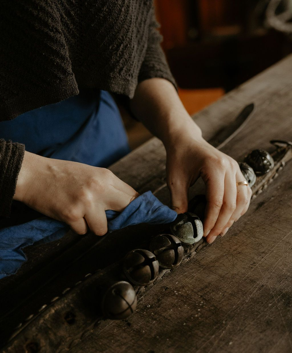 Des mains nettoient des clochettes sur une lanière de cuir posée sur une table en bois.
